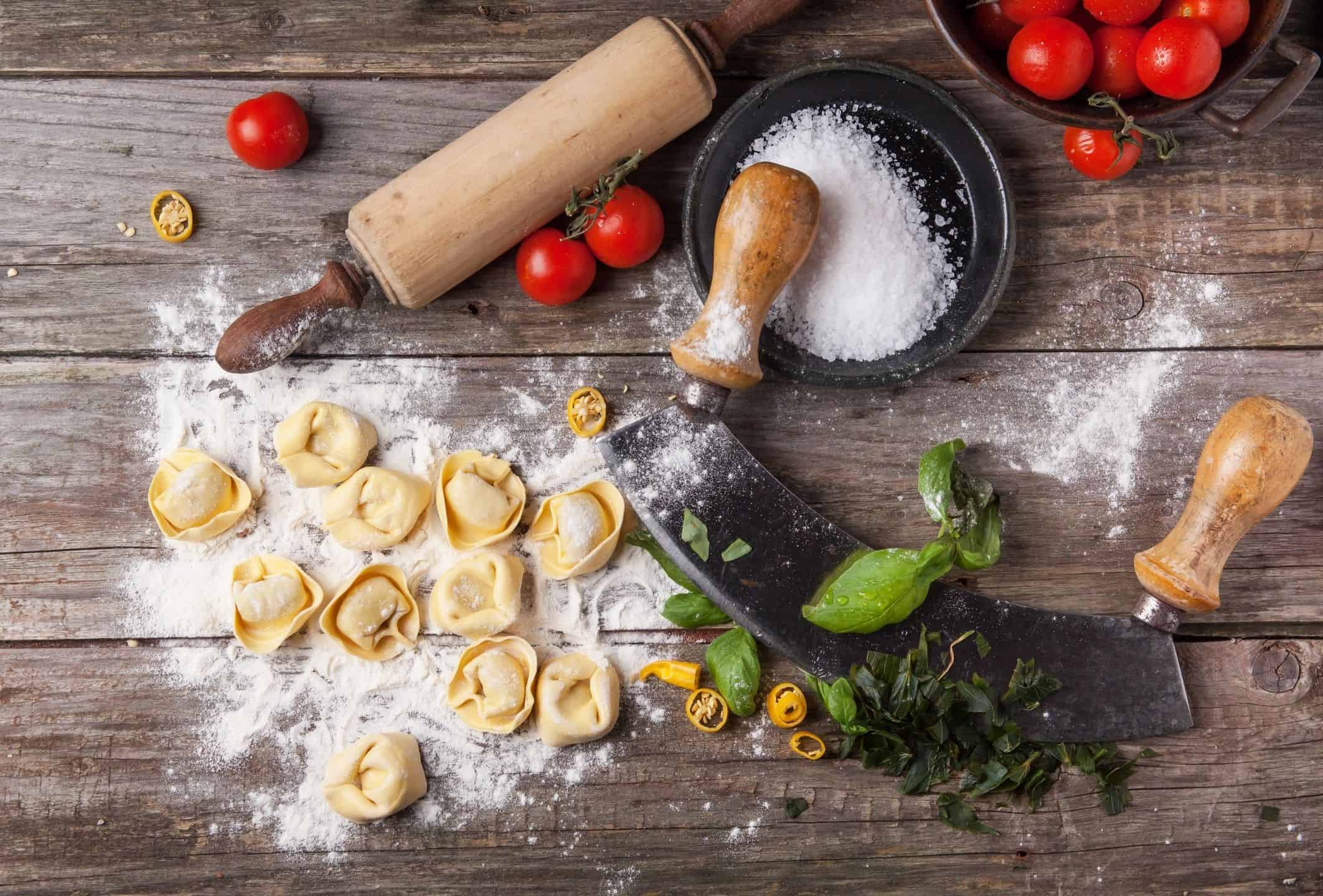Delicious homemade tortellini pasta with basil, cherry tomatoes, and cooking tools on rustic wooden.