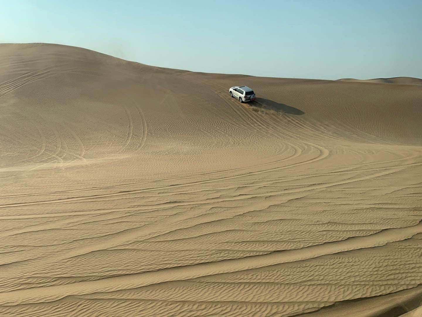 SUV driving on sand dunes in a desert landscape.