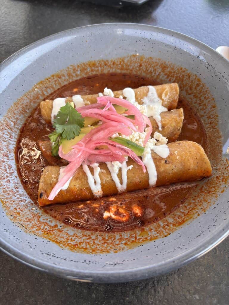 Delicious Mexican enchiladas topped with pink pickled onions, cilantro, and crumbled cheese, served.