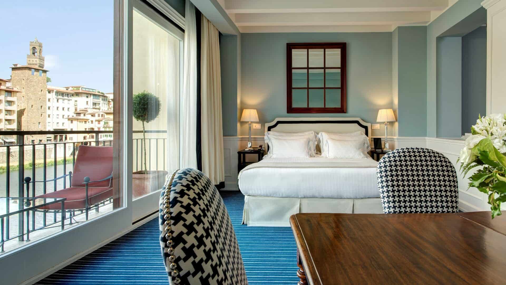 Luxury hotel room with balcony overlooking city skyline, modern decor, and comfortable bedding.