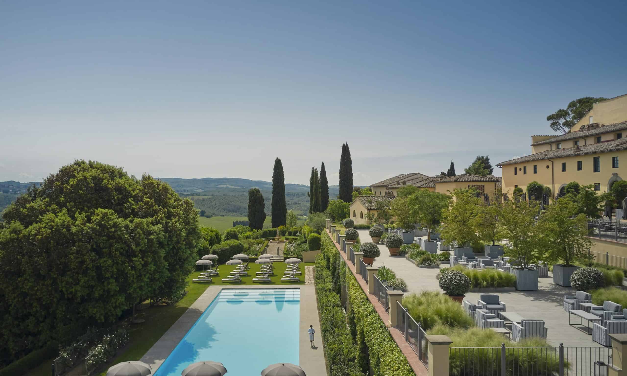 Luxury hotel pool with scenic Tuscan landscape, rolling hills, and elegant architecture in Italy.