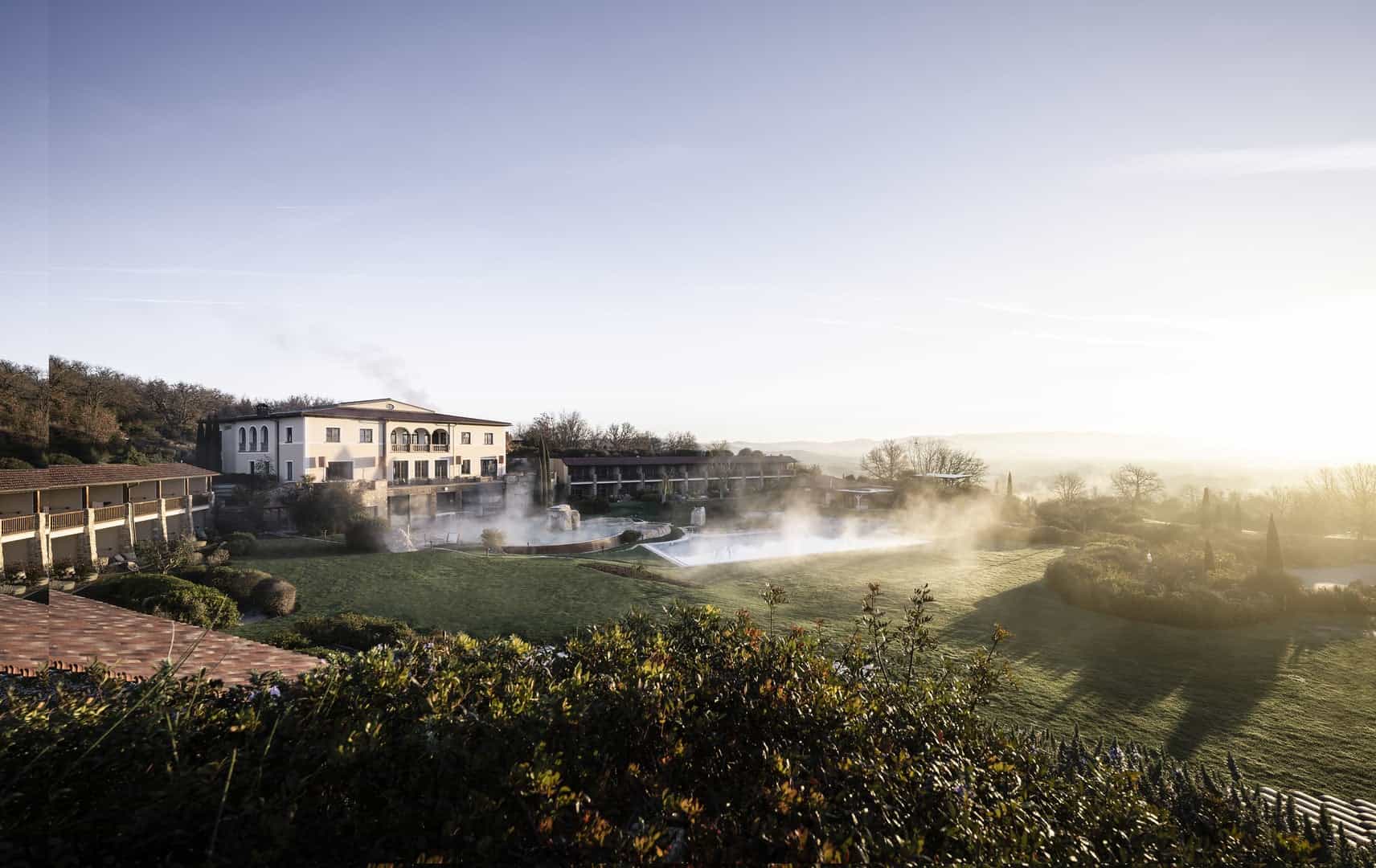 Hot springs with steam rising over lush green landscape and a building in the background, showcasing.