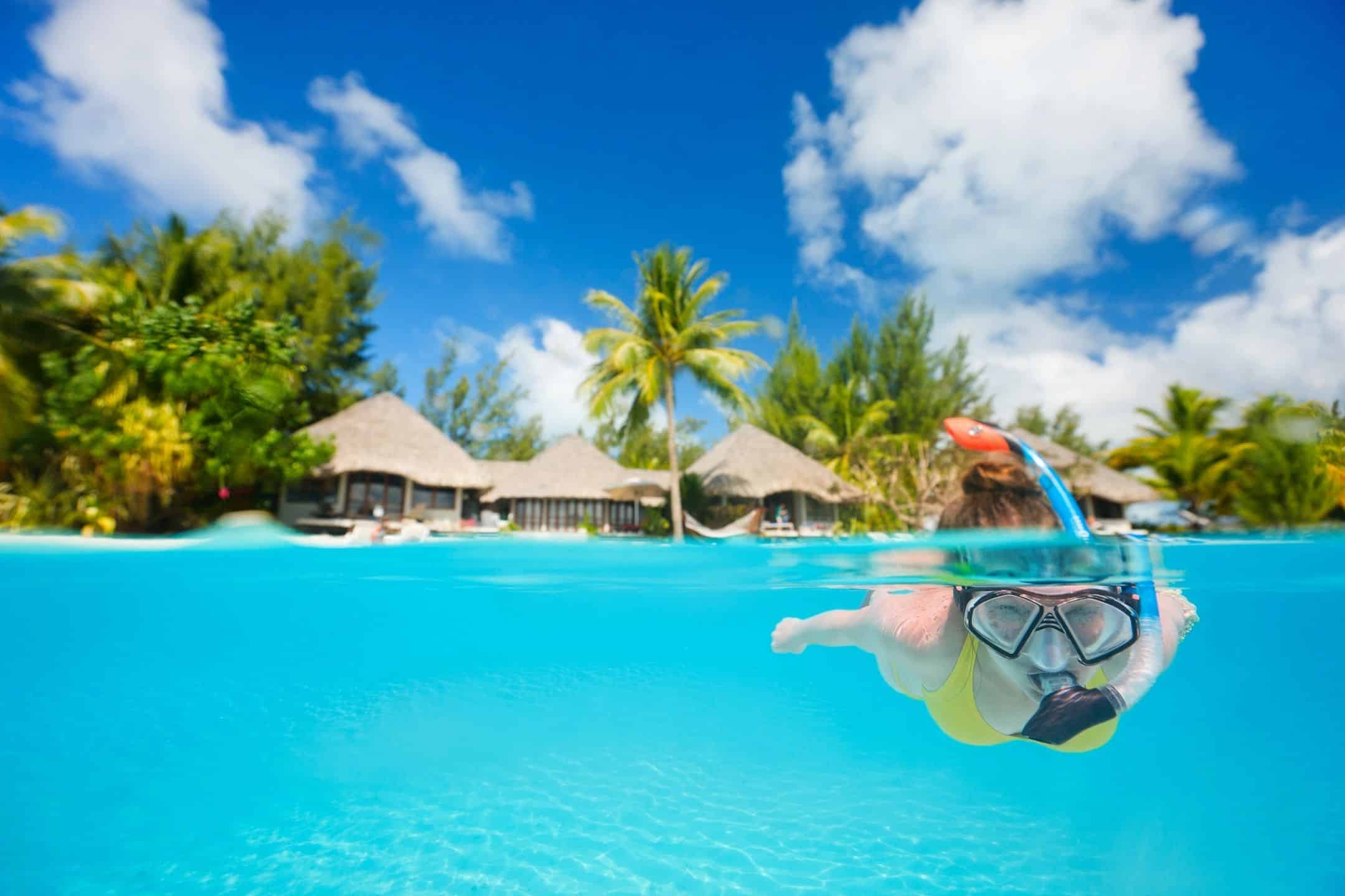 Overwater bungalow resort with snorkeler enjoying clear blue water and lush tropical surroundings.