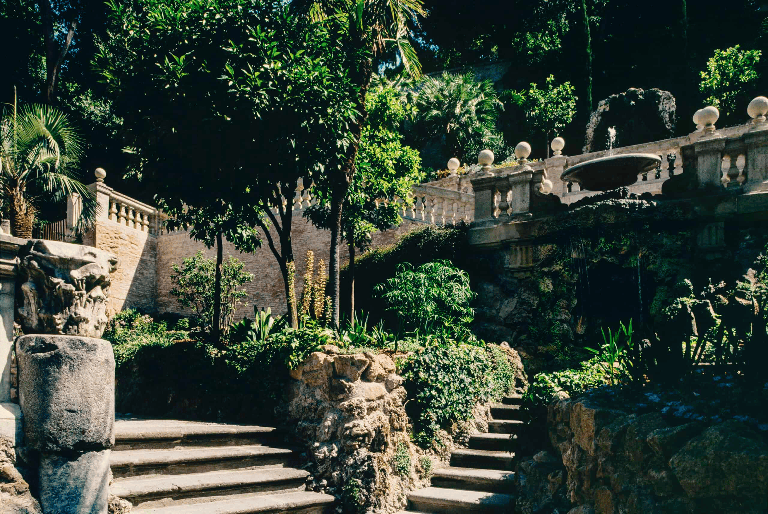 Elegant garden with stone stairs, lush trees, and decorative balustrades in a serene outdoor setting.