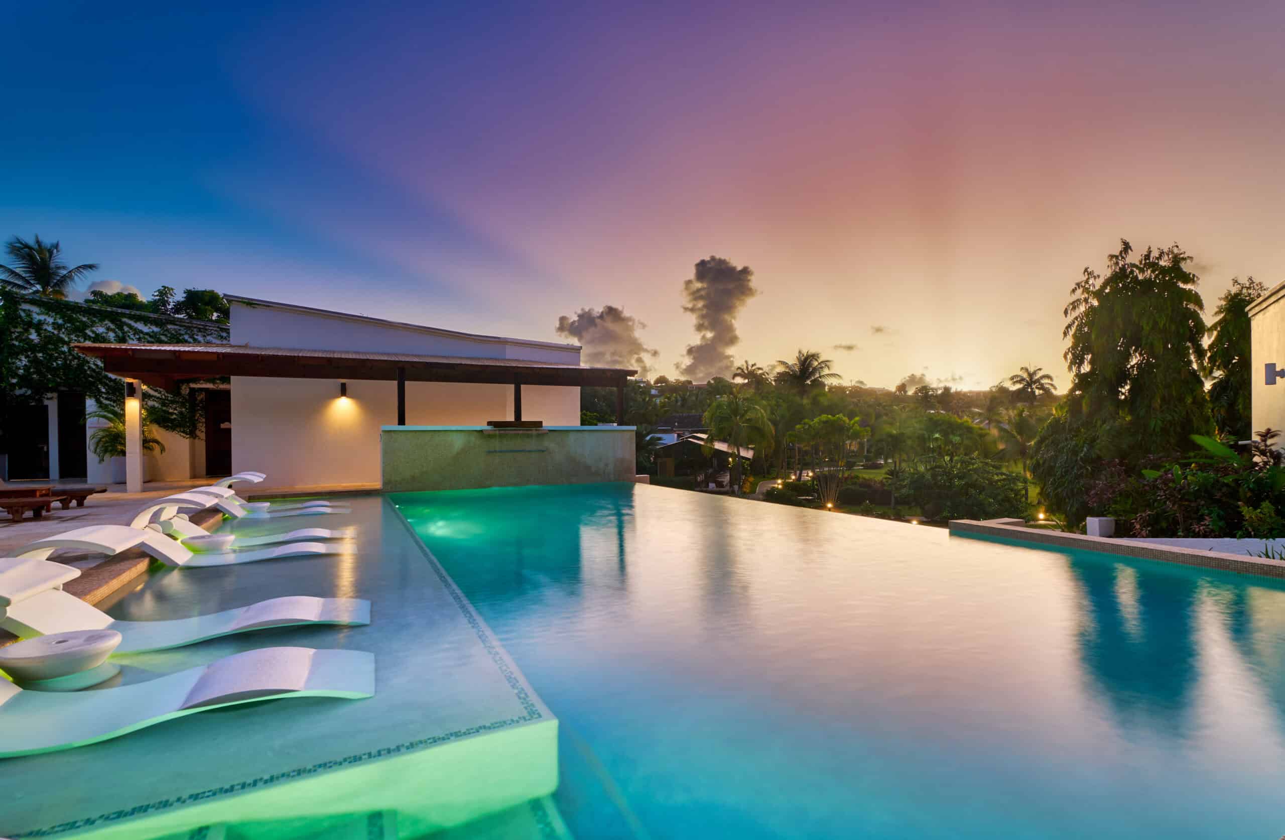 Infinity pool with sunset view in a tropical resort setting, surrounded by lush greenery and modern.