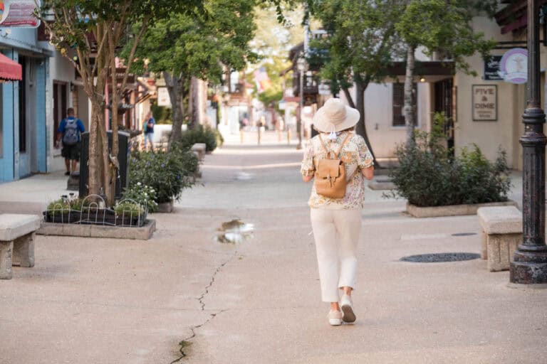 Woman walking on historic St. Augustine street with trees and shops.