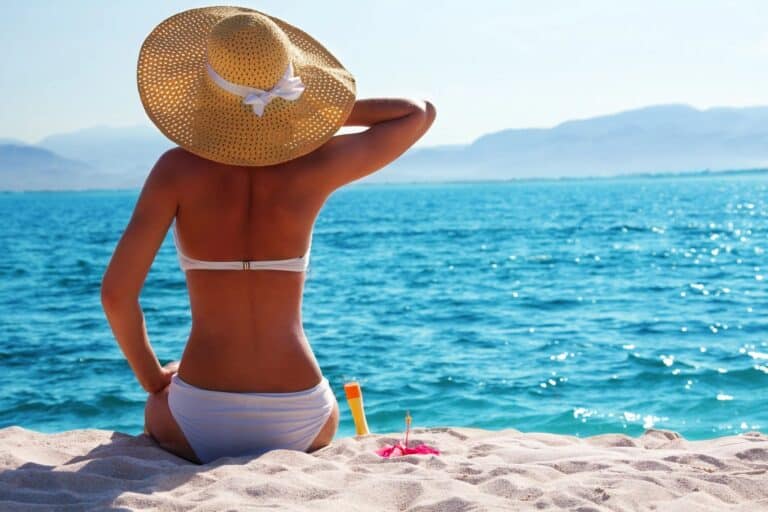 Woman relaxing on the beach with a wide-brimmed hat overlooking the ocean.
