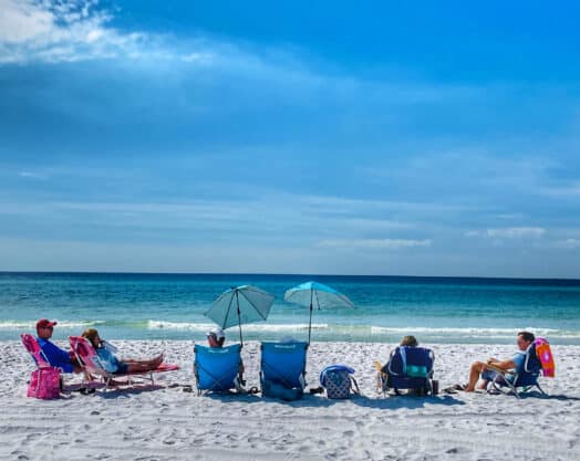 Beachgoers relaxing on Florida shoreline with umbrellas and chairs.