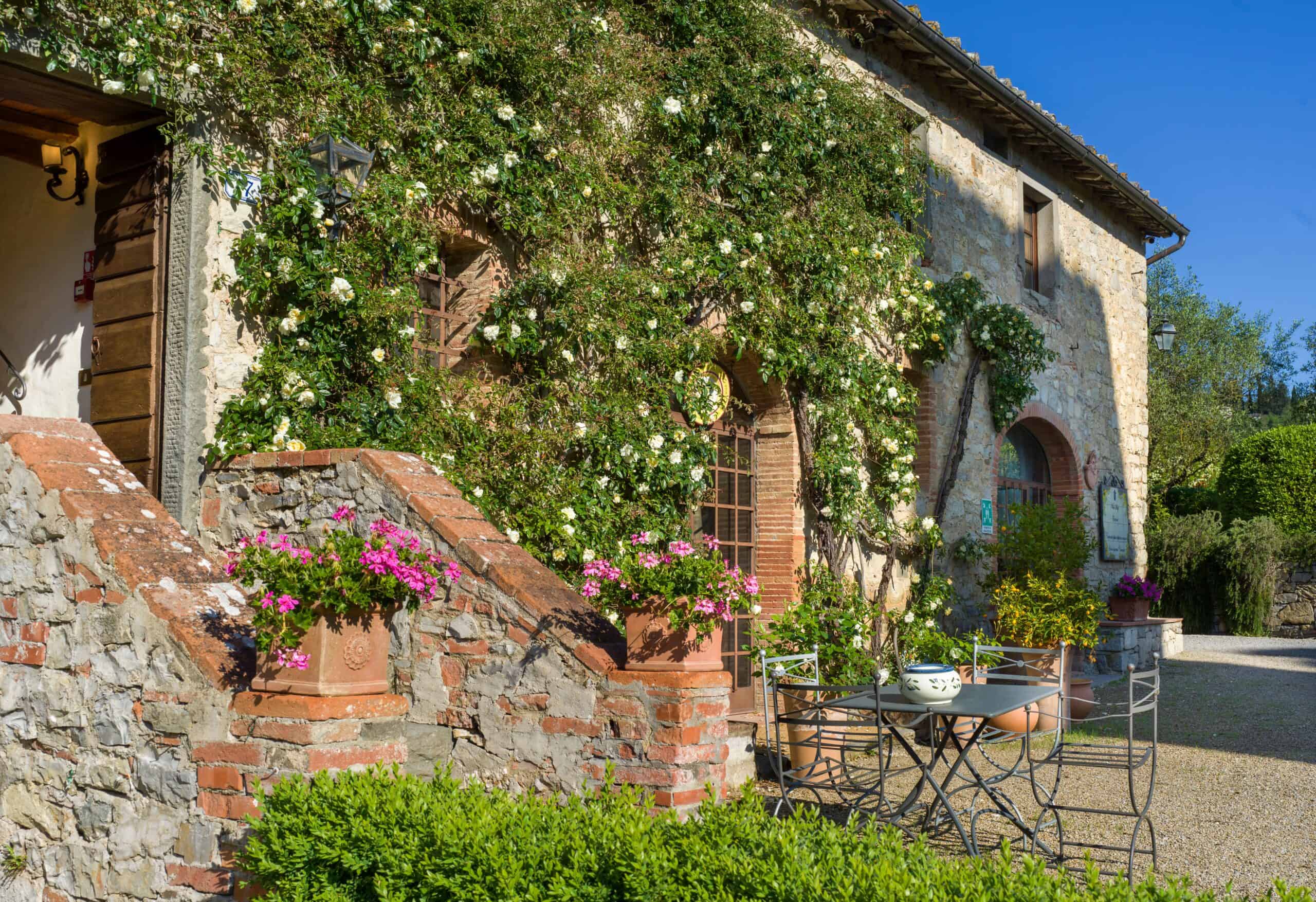 Rustic stone house with lush greenery and blooming flowers in Tuscany.