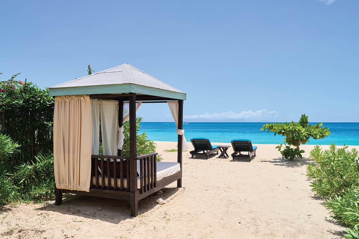 Beach cabana with curtains overlooking turquoise sea and sandy shore.