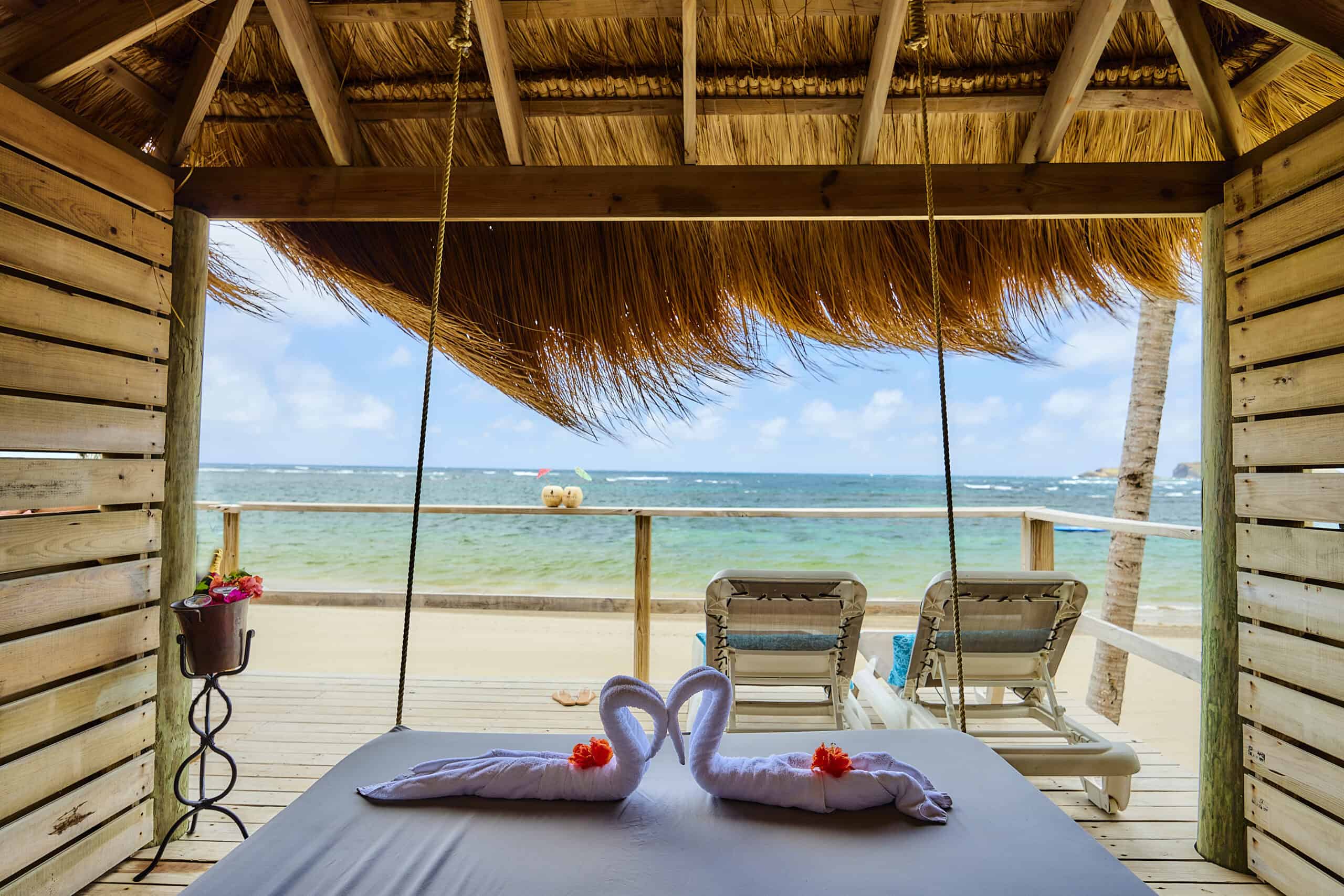 Beachside hut with swings, overlooking turquoise ocean and sandy beach.