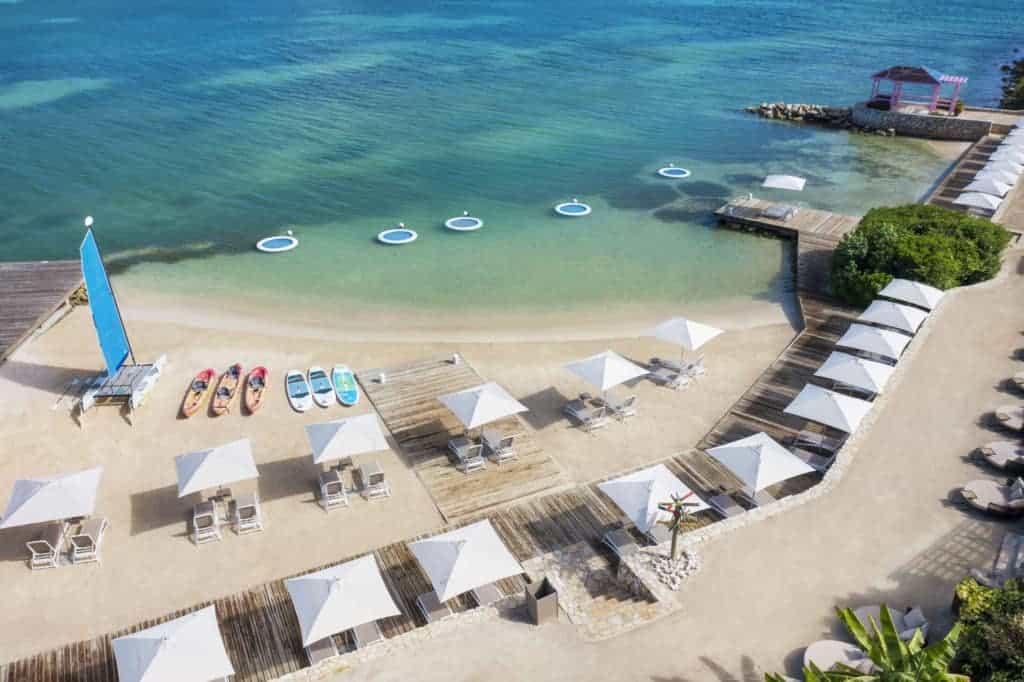 Beautiful tropical beach with lounge chairs, umbrellas, and paddleboarding options on clear blue wat.