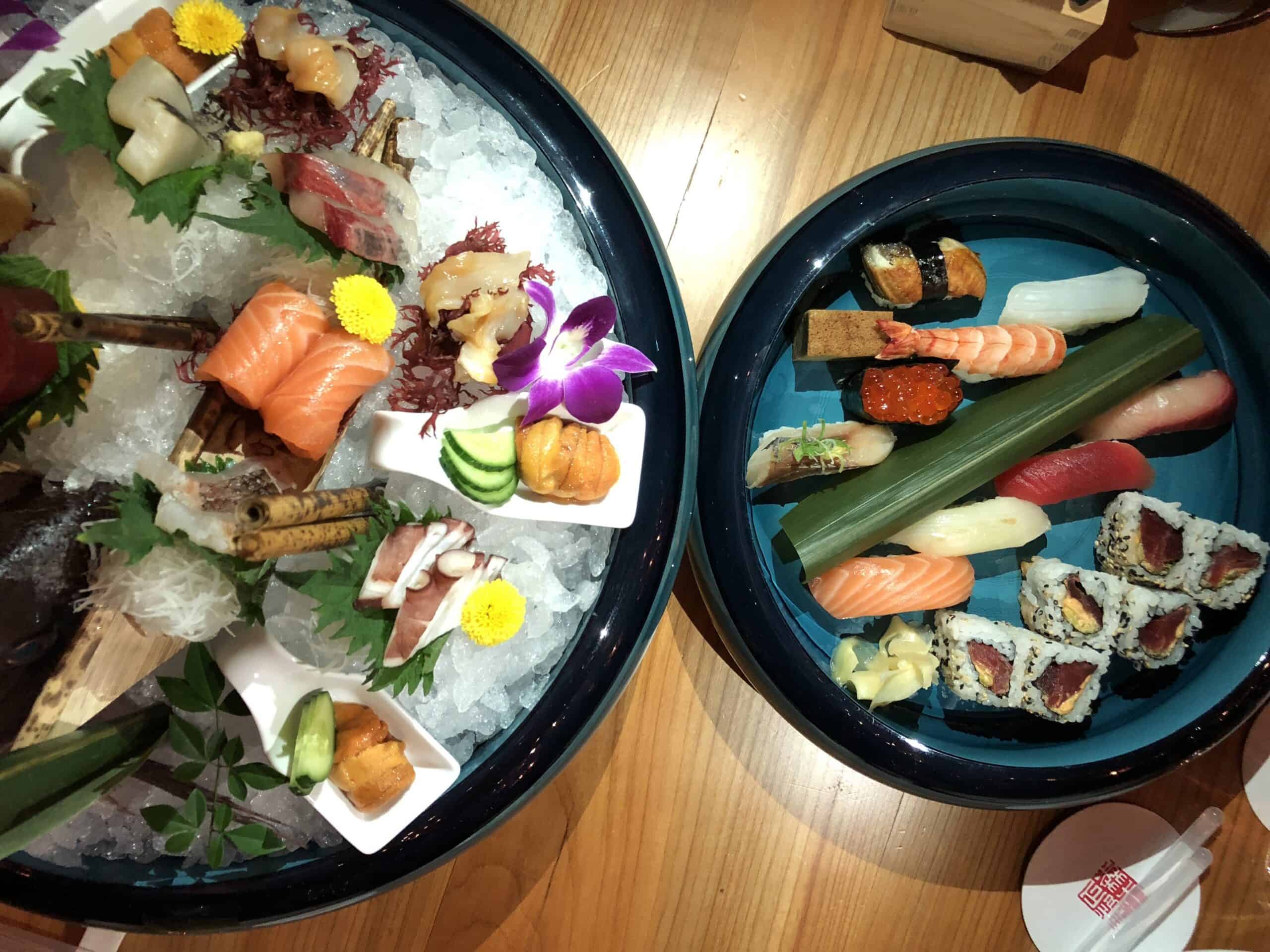 Sushi platter featuring assorted fresh fish, sashimi, and sushi rolls on ice and a wooden table.