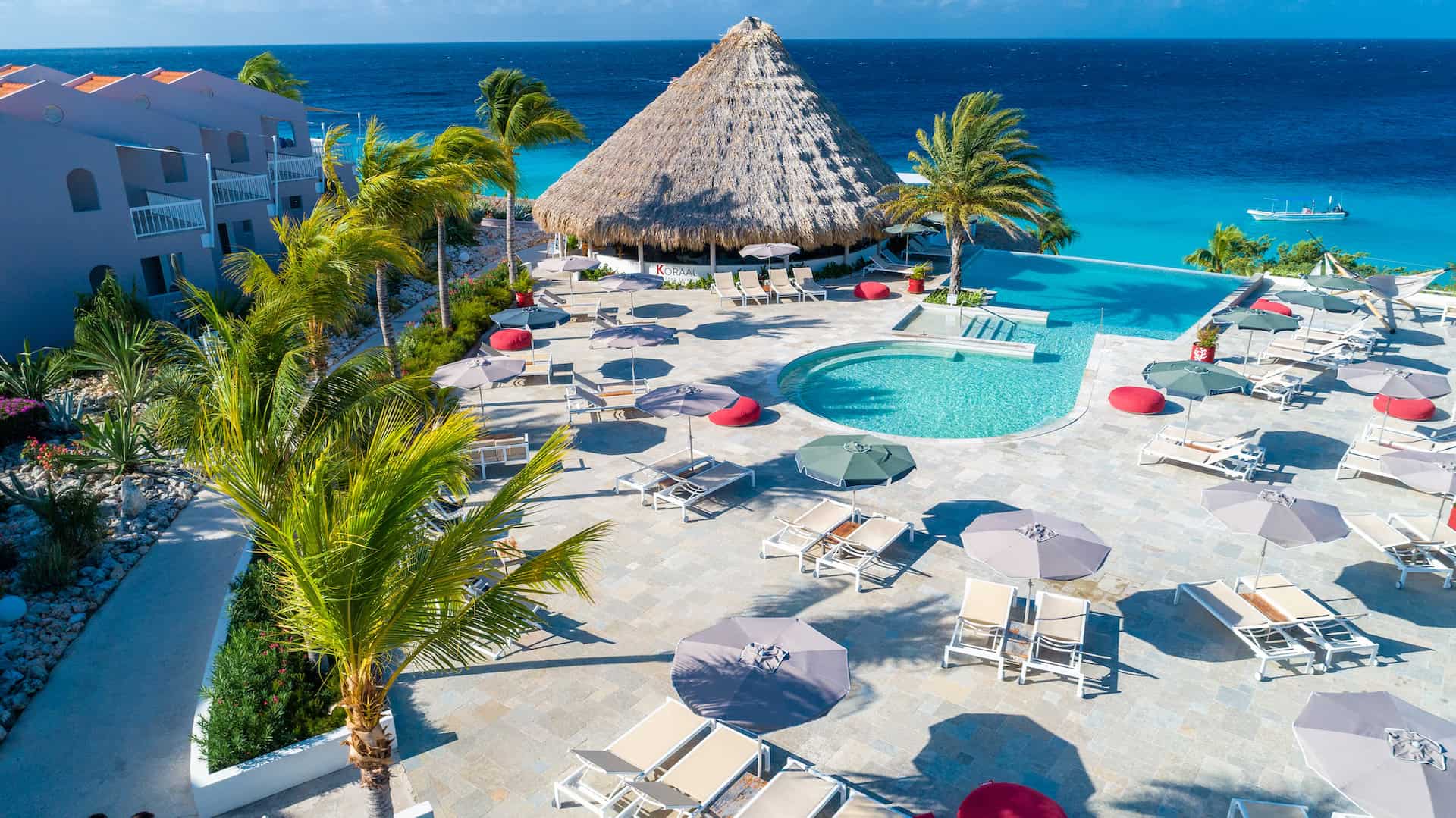 Beachside resort pool with thatched roof hut, palm trees, and ocean view for relaxation and travel i.