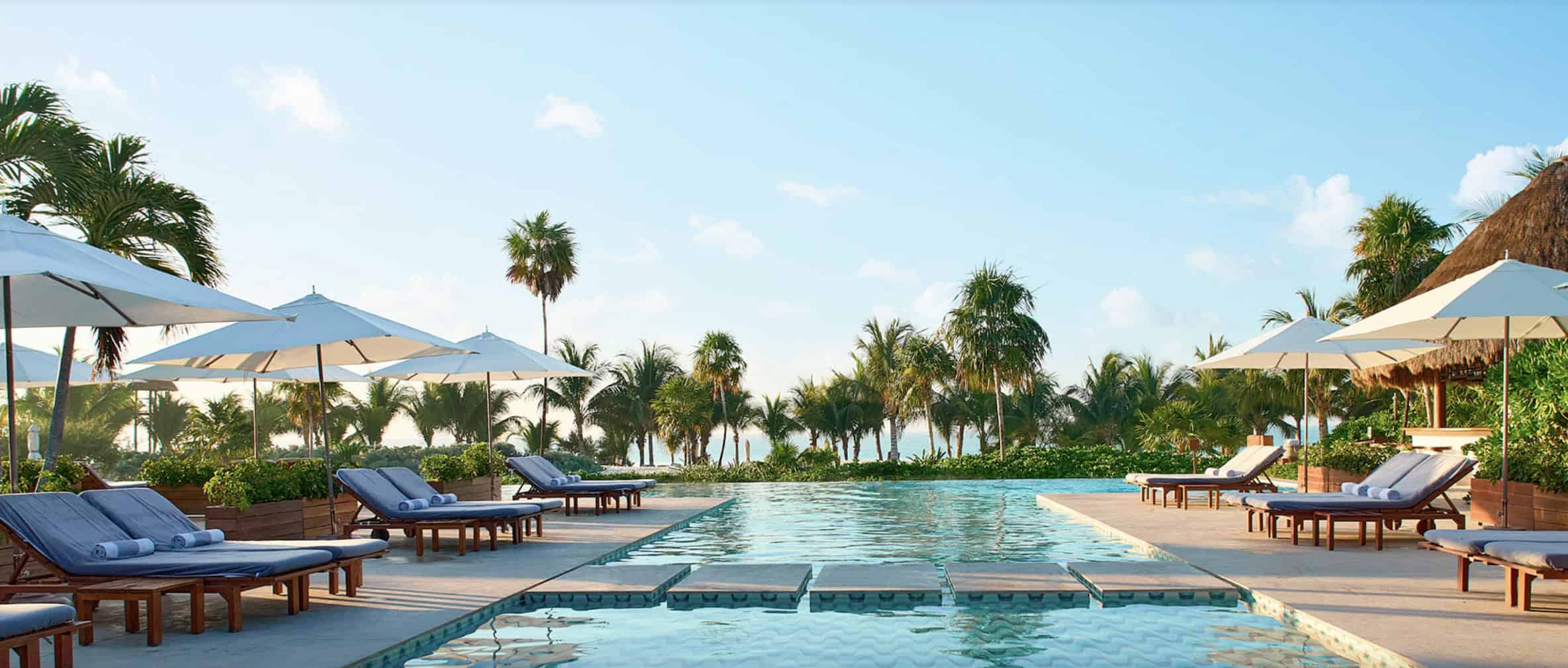 Luxury poolside resort in Riviera Maya with palm trees and sun loungers.