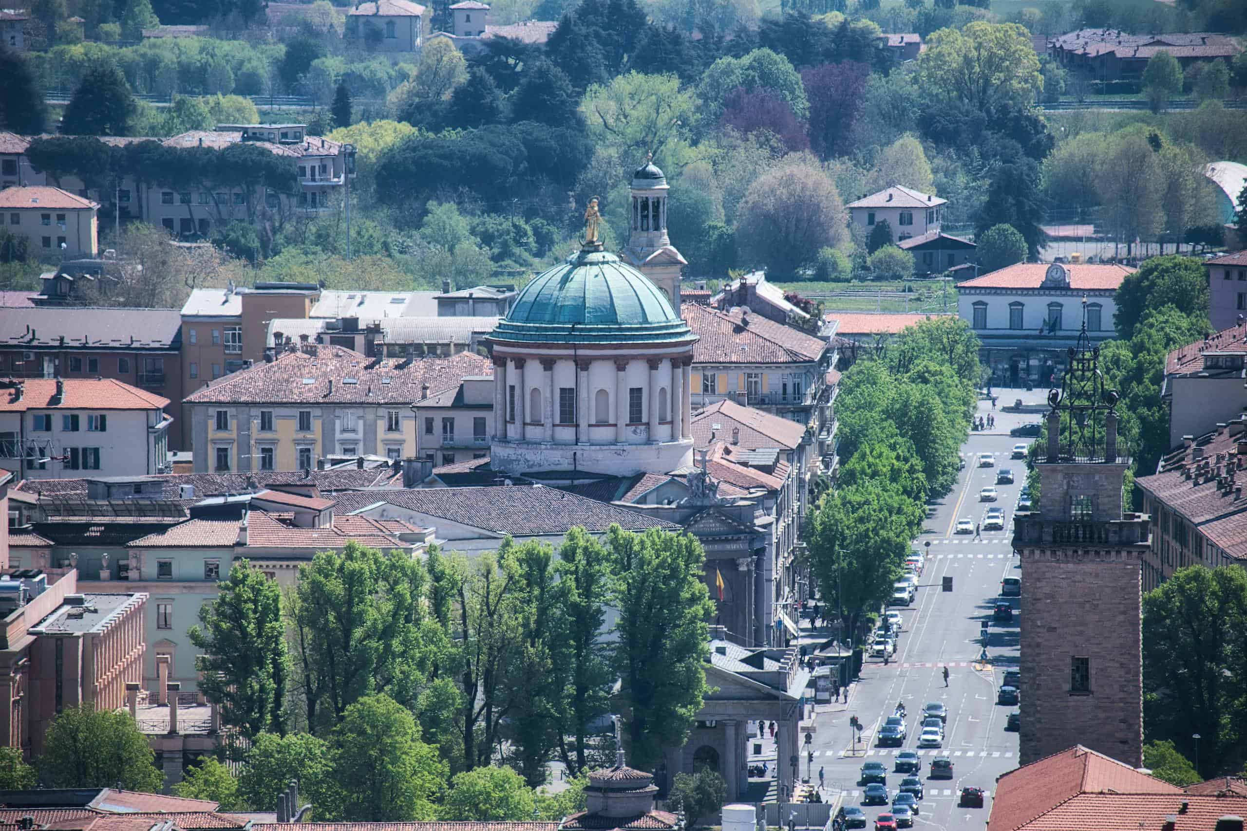 Historic Italian cityscape featuring a prominent domed church, tree-lined streets, and classic archi.