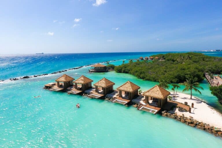 Overwater bungalows on turquoise Caribbean waters with lush greenery and clear skies.