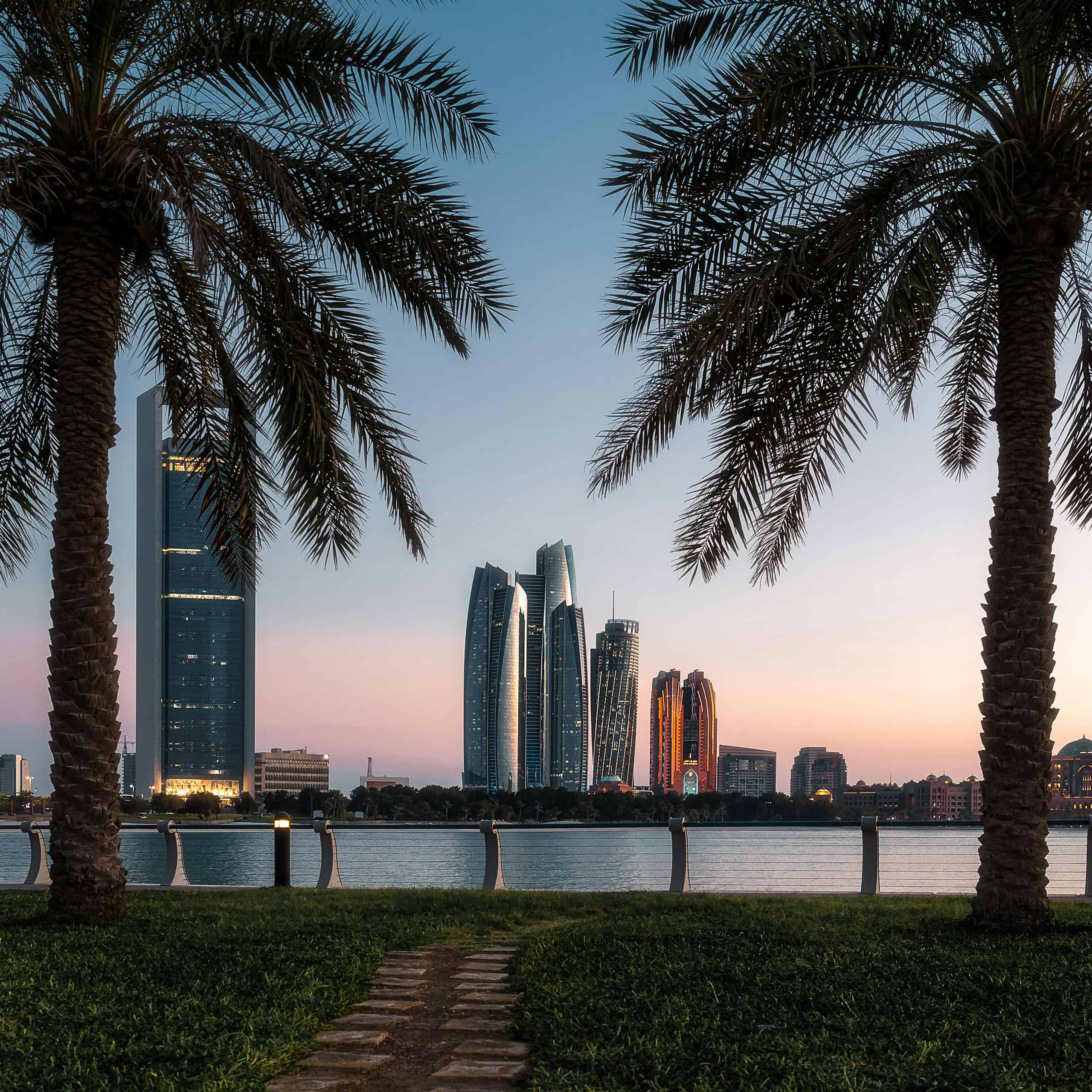 Dubai skyline with modern skyscrapers and waterfront at sunset, featuring palm trees in the foregrou.