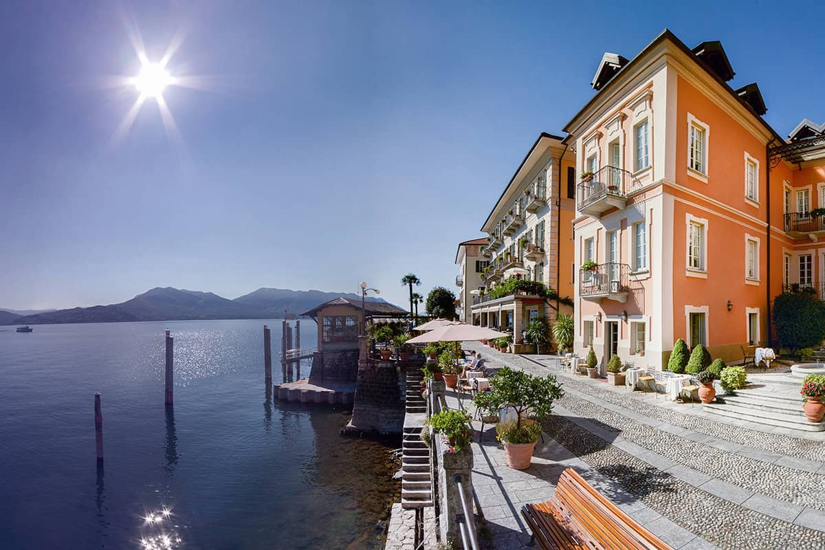 Lakeside hotel on Lake Maggiore featuring vibrant buildings, outdoor seating, and mountain backdrop.
