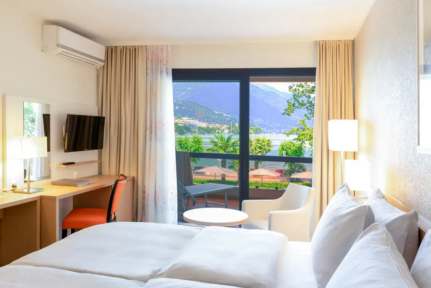 Comfortable hotel room overlooking Lake Maggiore and surrounding mountains, featuring modern ameniti.