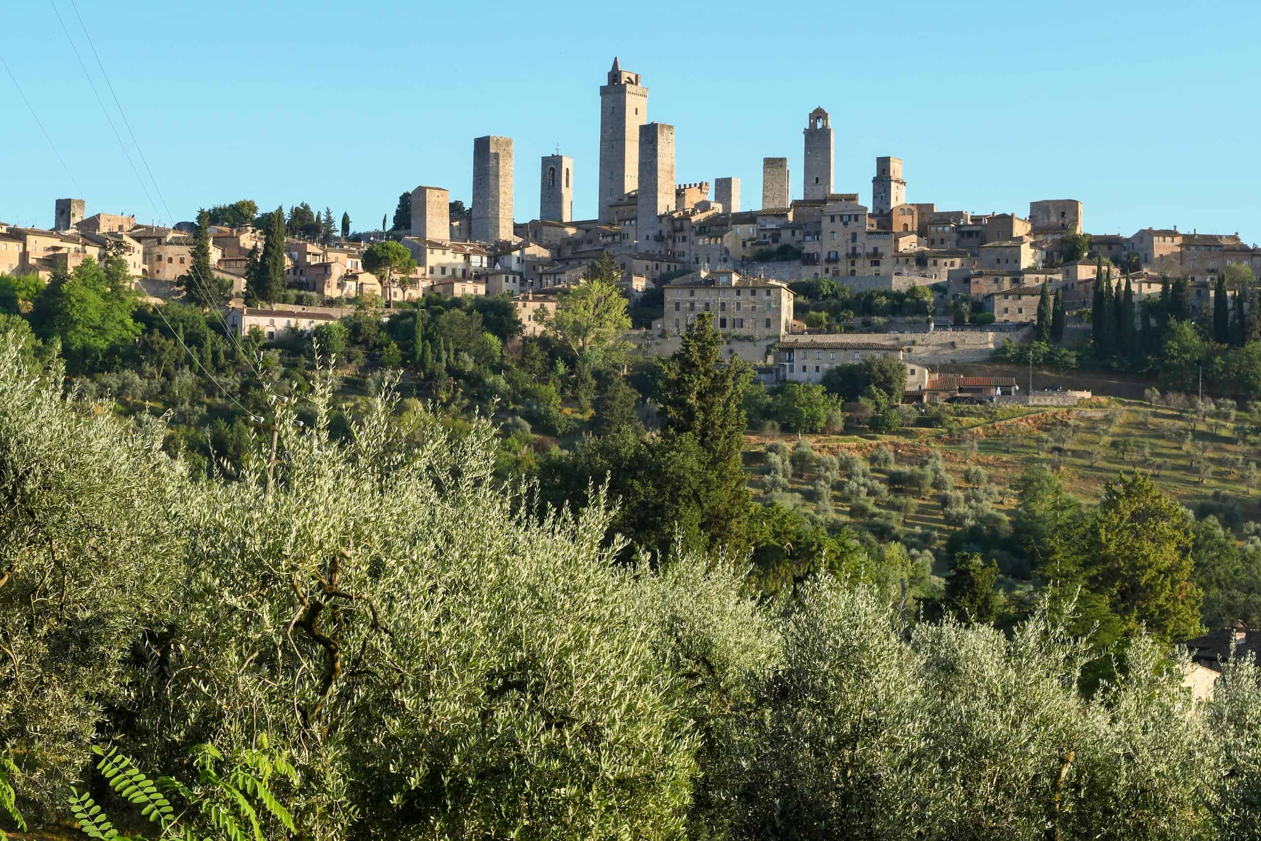 Ancient hilltop town with medieval towers and lush greenery in Italy, showcasing historic architectu.