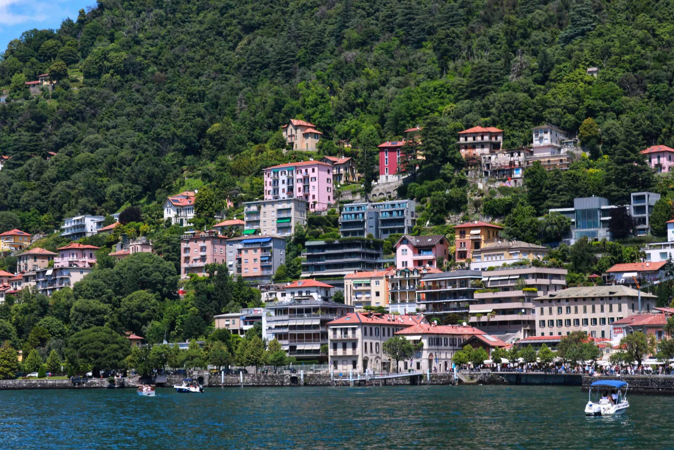 Scenic view of colorful lakeside buildings on Lake Como, Italy, with lush green hills in the backgro.