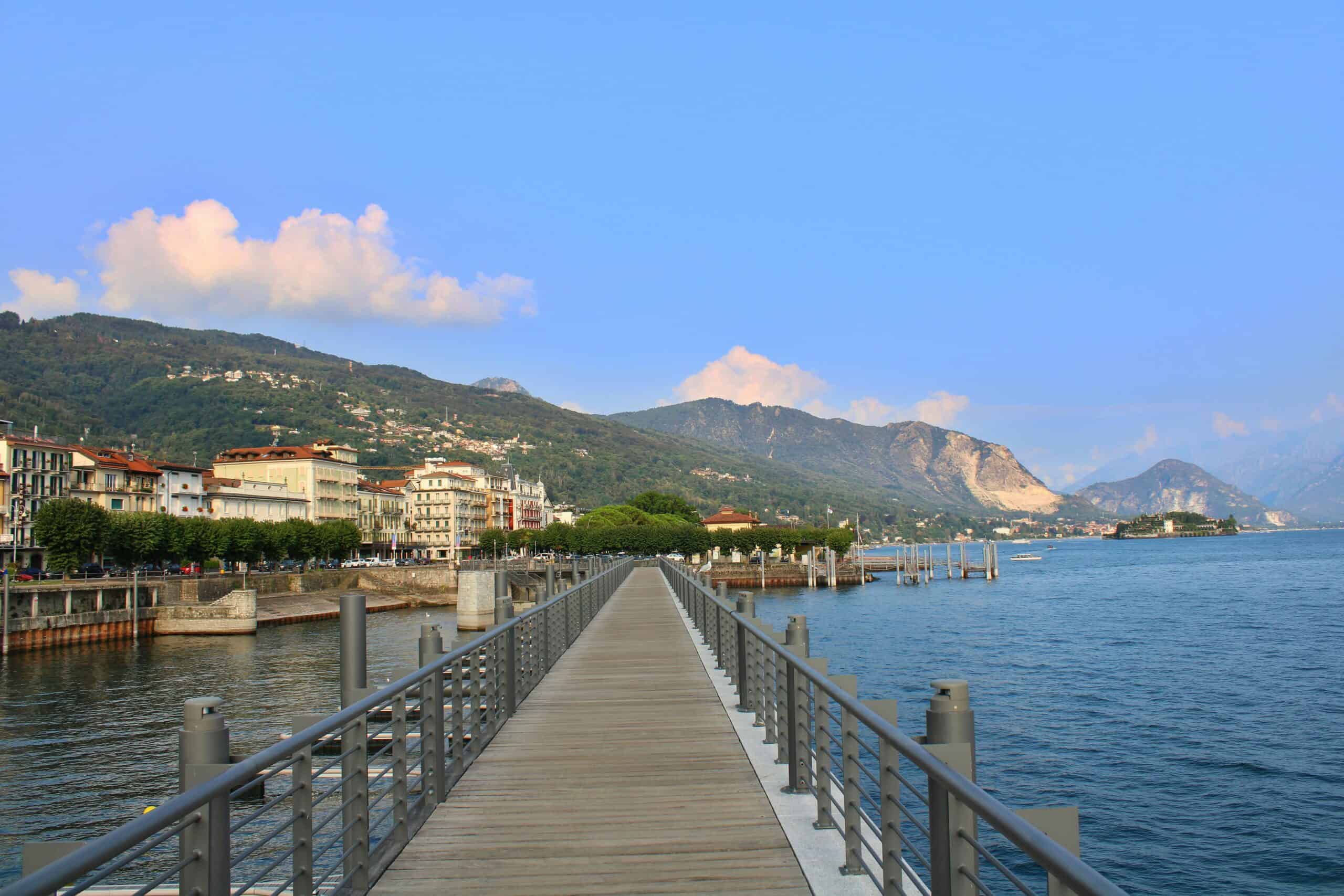 Scenic lakeside walkway in a coastal town with mountains, water, and clear blue sky, perfect for tra.