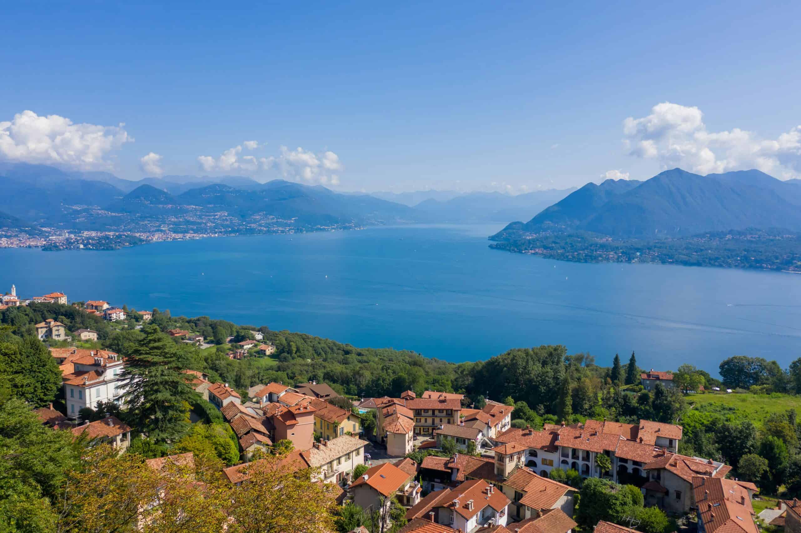 Breathtaking view of a serene lake surrounded by mountains and charming hillside homes under a clear.