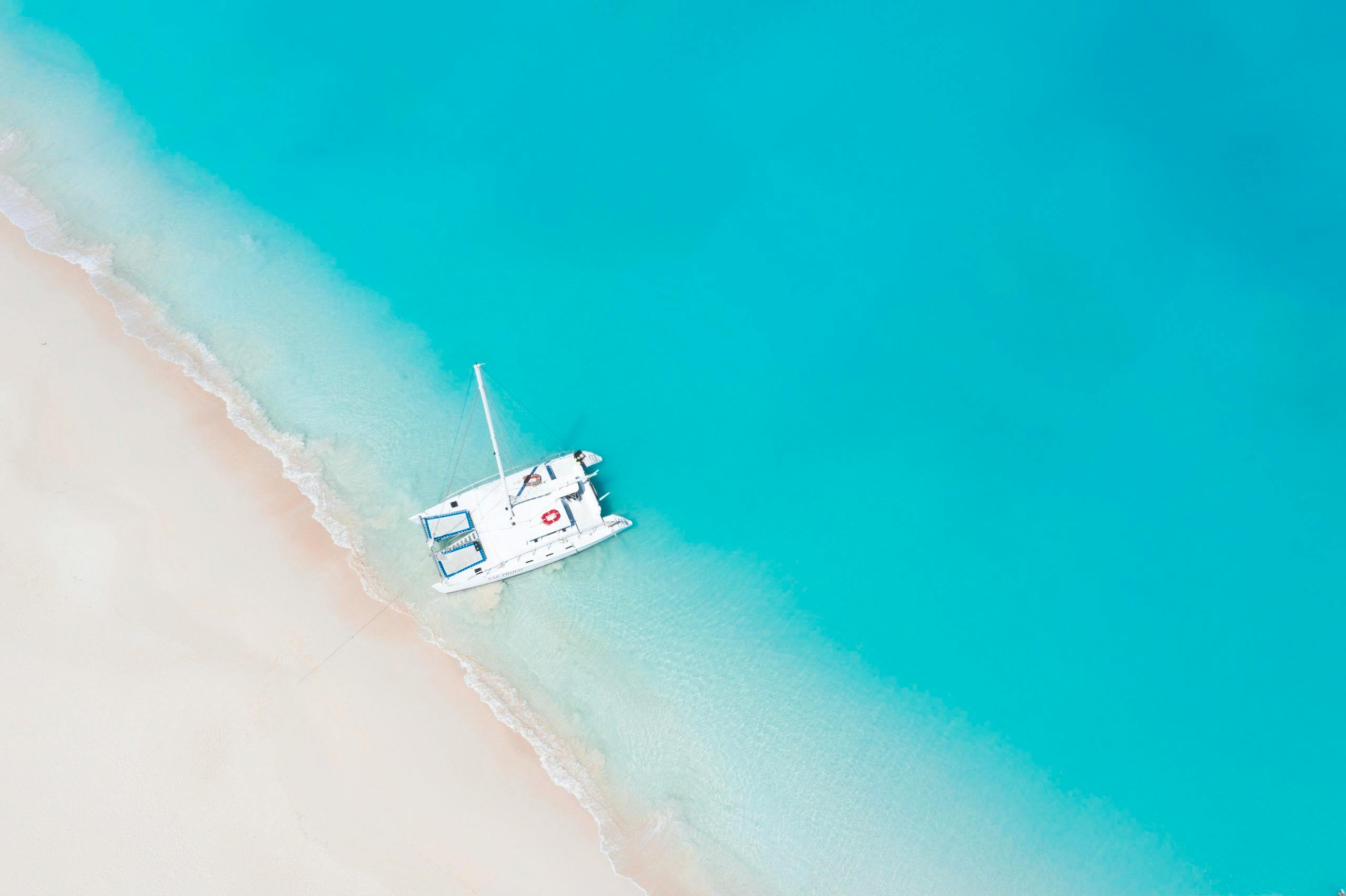 Drone shot of a white boat on a pristine beach with clear turquoise waters.