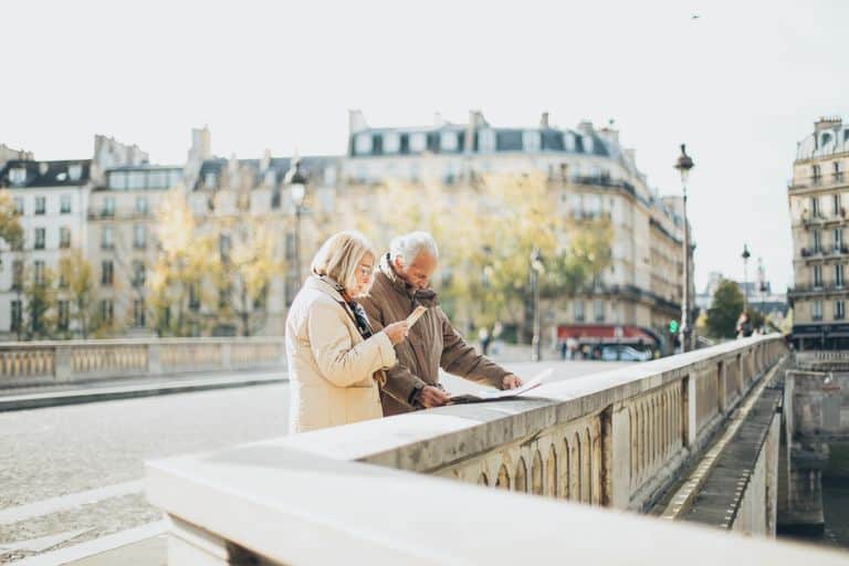 Elderly couple sightseeing on a bridge in Paris, enjoying the cityscape.