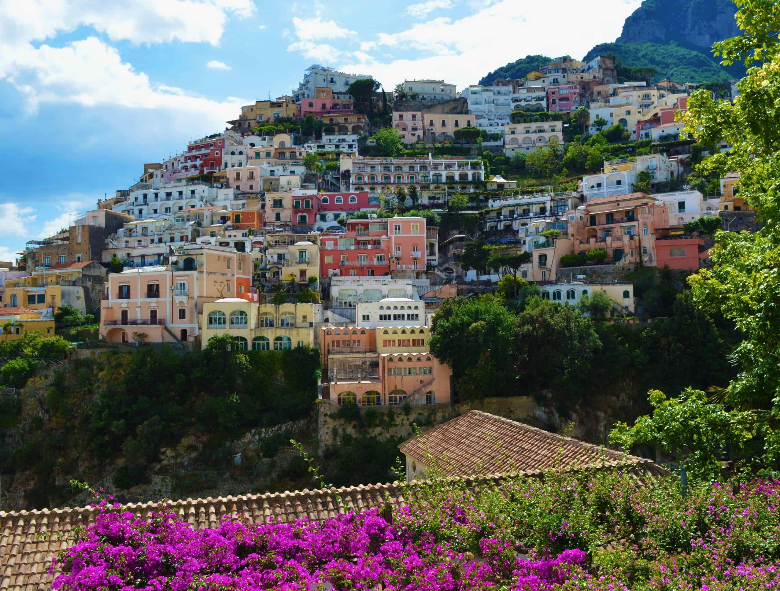 Vibrant hillside houses in Amalfi Coast with lush greenery and mountains.