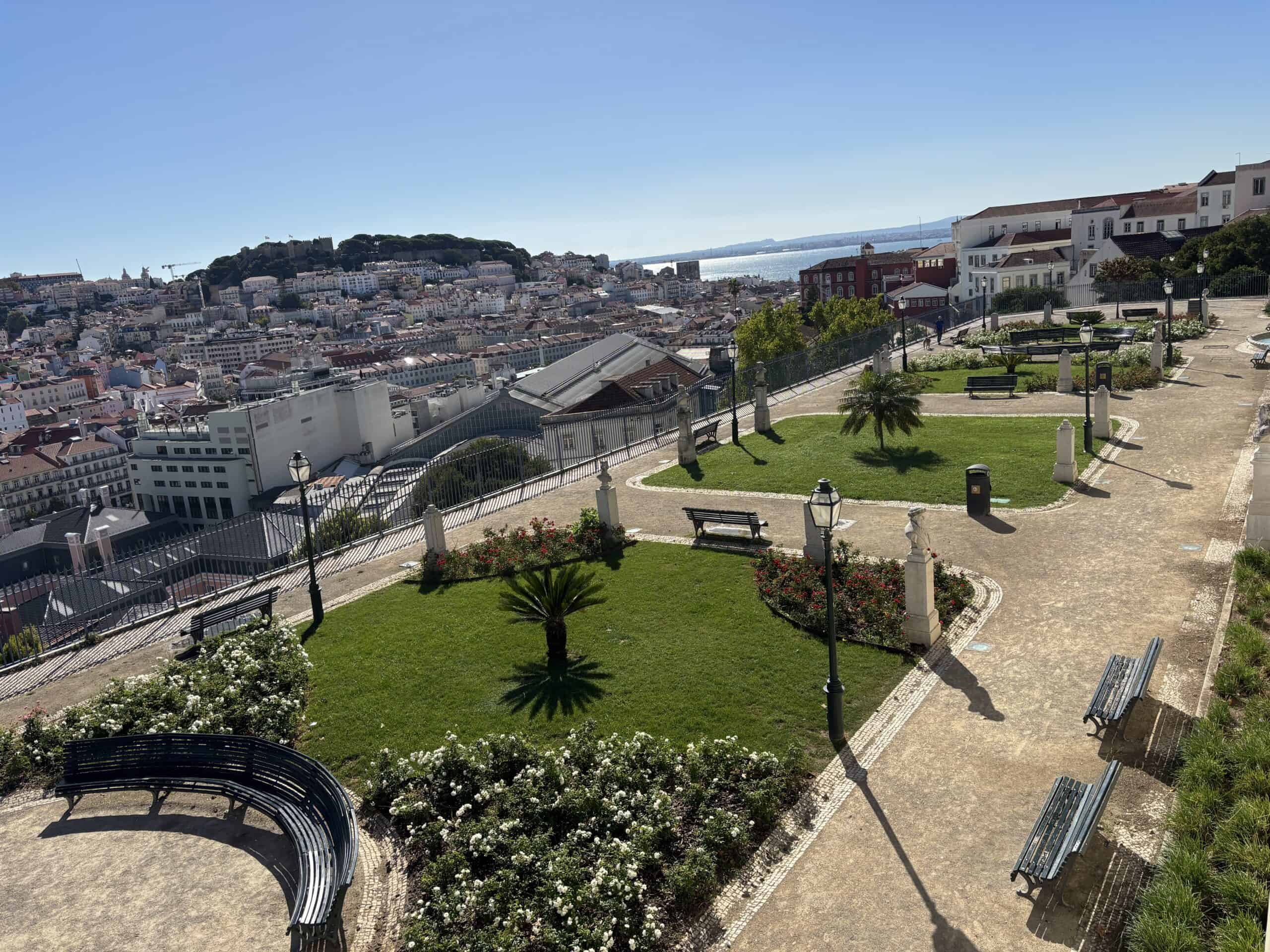 Panoramic view of Lisbon cityscape from a hilltop park with benches and greenery.