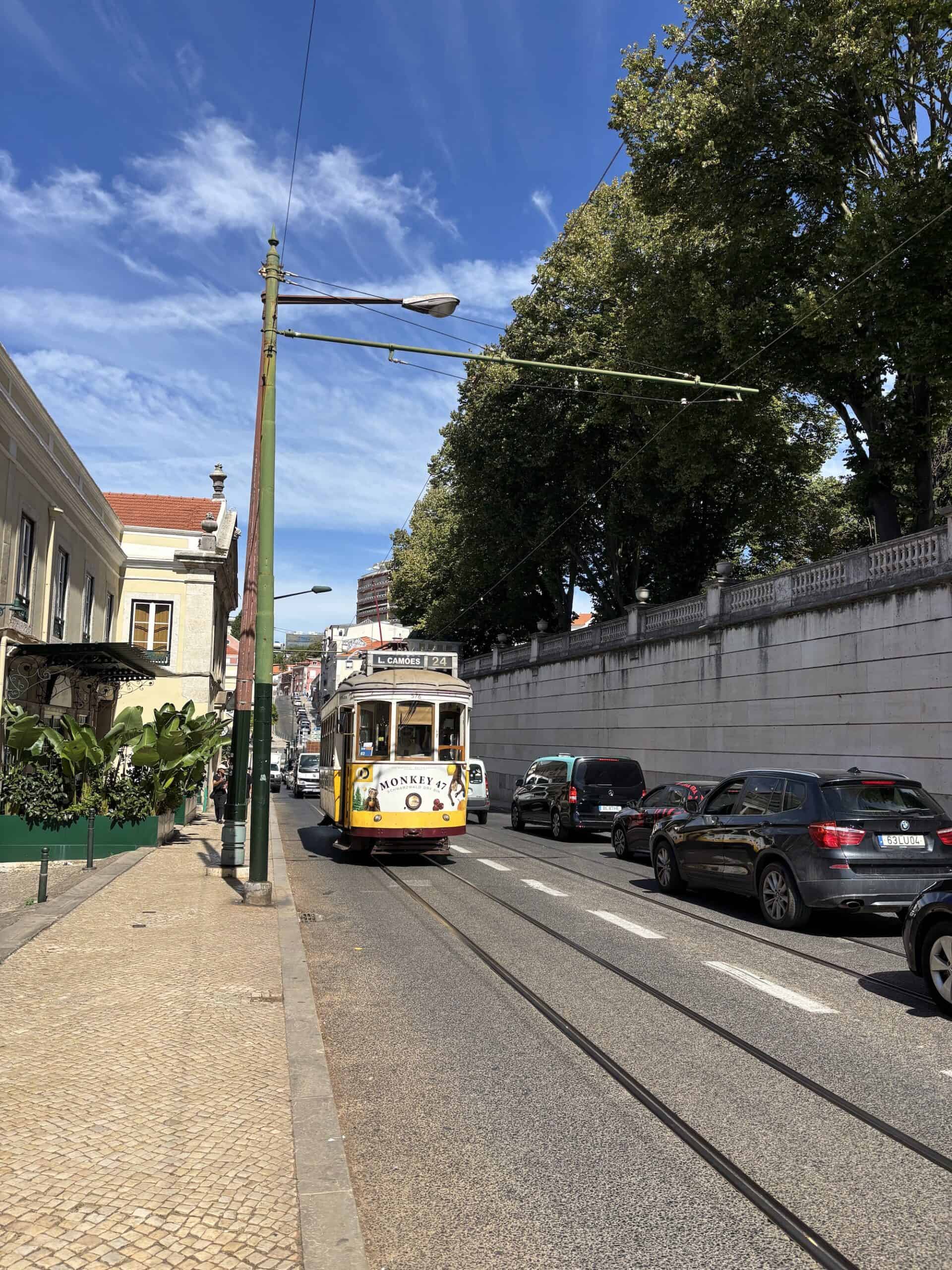 Historic yellow tram on city street with cars and trees in Lisbon.